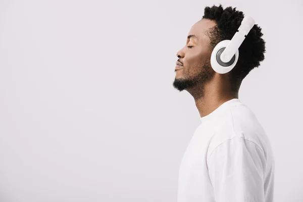 Vue latérale de l'homme afro-américain heureux écoutant de la musique dans les écouteurs sur blanc — Photo de stock