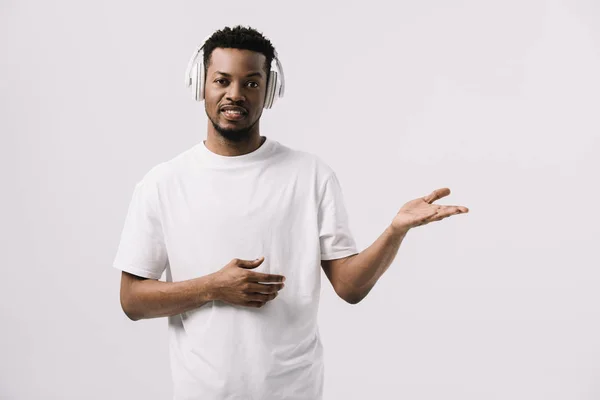 Веселий афроамериканський чоловік слухає музику в навушниках і жестикулює ізольовано на білому — стокове фото