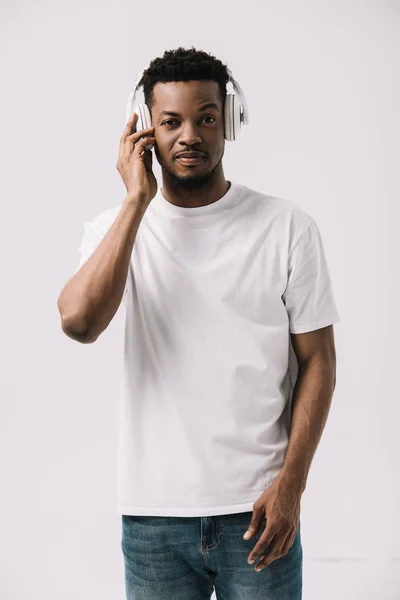 Hombre afroamericano guapo escuchando música y tocando auriculares aislados en blanco - foto de stock