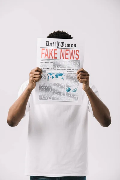 Афроамериканський чоловік прикриває обличчя під час читання газети з фальшивими новинами, написання ізольовано на білому — стокове фото