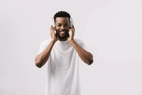 Hombre afroamericano feliz sonriendo y tocando auriculares aislados en blanco - foto de stock