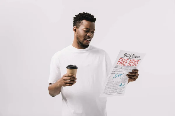 Bel homme afro-américain tenant une tasse en papier et lisant un journal avec de fausses nouvelles lettrage isolé sur blanc — Photo de stock