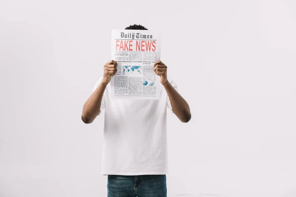 Afro-américain homme couvrant visage tout en tenant journal avec de fausses nouvelles lettrage isolé sur blanc — Photo de stock
