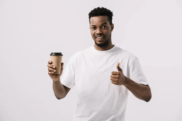 Hombre afroamericano feliz sosteniendo taza de papel y mostrando el pulgar hacia arriba aislado en blanco - foto de stock