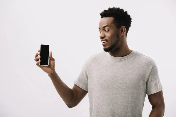 Hombre afroamericano feliz mirando el teléfono inteligente con pantalla en blanco aislado en blanco - foto de stock