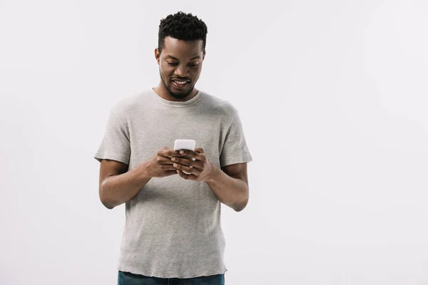 Hombre americano africano alegre en camiseta gris usando el teléfono inteligente aislado en blanco - foto de stock