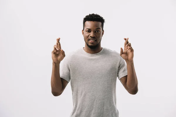 Worried african american man standing with fingers crossed isolated on white — Stock Photo