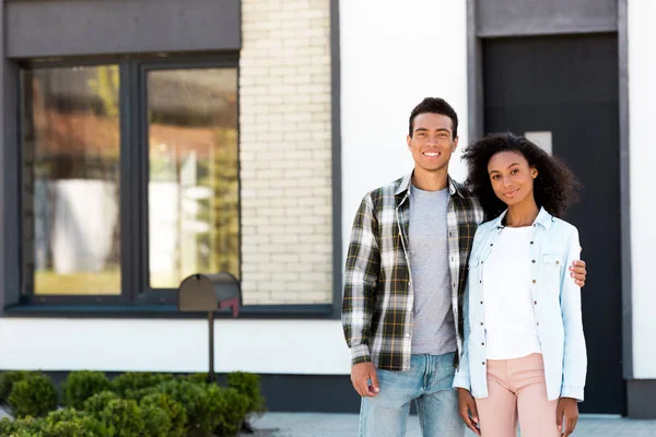 Africano americano marido y esposa de pie cerca de nuevo casa y mirando la cámara - foto de stock