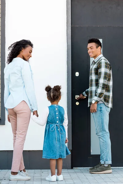 Vista de cuerpo entero del padre afroamericano abriendo la puerta mientras la madre y el niño caminan al hombre - foto de stock