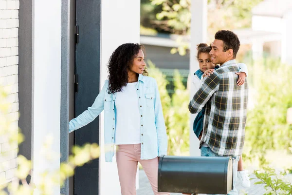 Selective focus of mother opening door of new house while african american father holding kid — Stock Photo