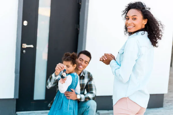 Afro-américaine femme debout près de l'homme et regardant la caméra tandis que père étreignant fille et tenant la clé — Photo de stock