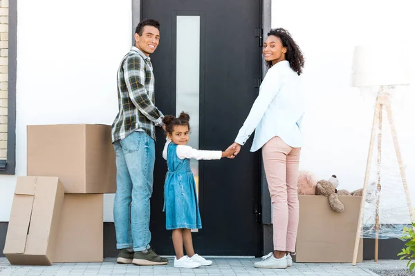 Vue pleine longueur de la famille afro-américaine regardant la caméra tout en se tenant devant la porte de la nouvelle maison — Photo de stock