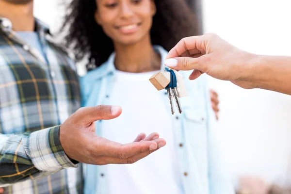 Vista ritagliata della donna afro-americana dando la chiave della nuova casa alla coppia felice — Foto stock