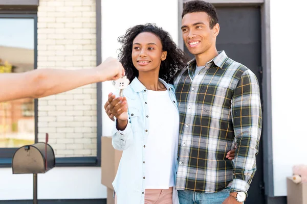 Couple afro-américain regardant femme et souriant tout en prenant la clé de la nouvelle maison — Photo de stock
