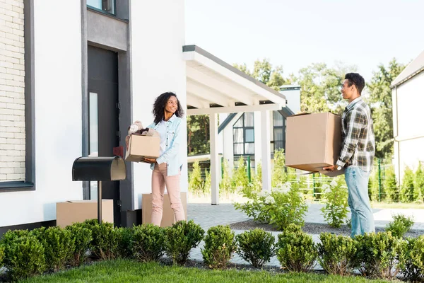 Vista completa de la pareja afroamericana caminando a casa y sosteniendo cajas - foto de stock