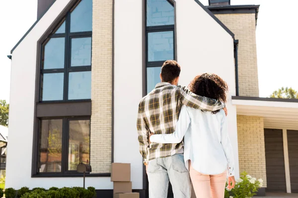 Visão traseira do casal afro-americano abraçando enquanto olha para a nova casa — Fotografia de Stock