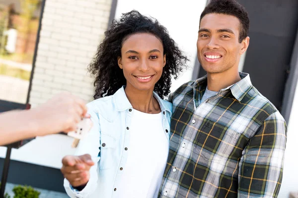 Селективный фокус африканской американской пары, смотрящей в камеру и улыбающейся, принимая ключ от нового дома — стоковое фото