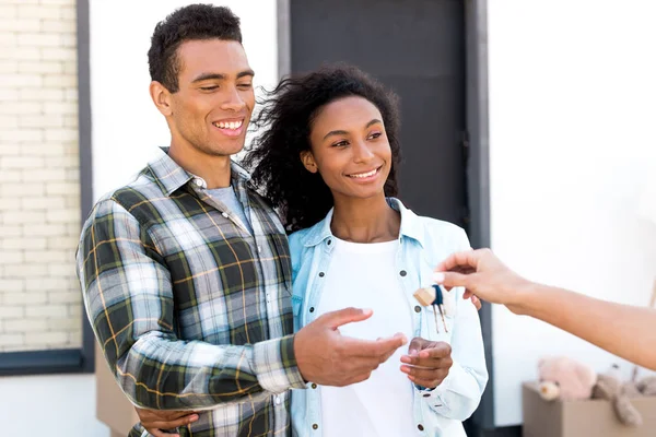 Selective focus of african american couple looking at woman and smiling while taking key of new house — Stock Photo