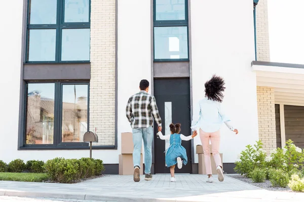 Vue arrière du couple afro-américain avec enfant courant vers une nouvelle maison — Photo de stock