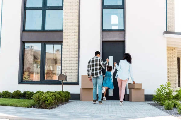 Vista completa de los padres afroamericanos tomados de la mano con el niño y caminando a la nueva casa - foto de stock