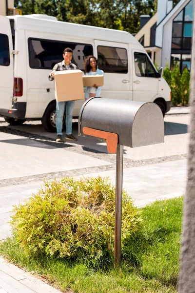 Messa a fuoco selettiva della cassetta postale e della coppia afro-americana che tiene le scatole mentre in piedi vicino all'auto — Foto stock