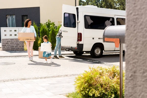 Selective foucs of african american mother and kid smiling while running to house with some stuff — Stock Photo