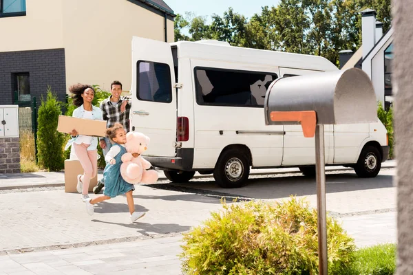 Full length view of african american mother and kid smiling and running to house while father looking at child and woman — Stock Photo