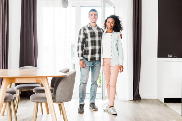 Vista completa de afroamericano marido y mujer abrazando y mirando a la cámara - foto de stock