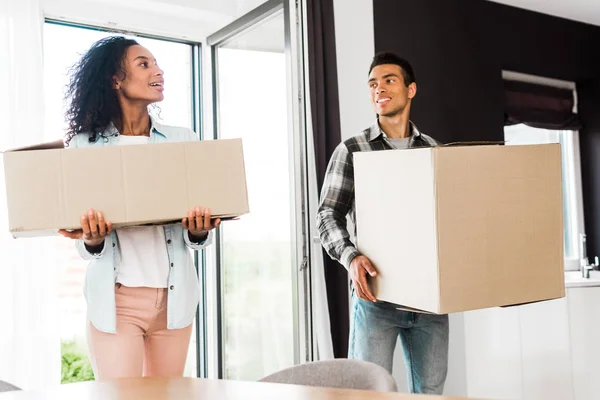 African american husband and wife holding boxes and looking at each other while walking into house — Stock Photo