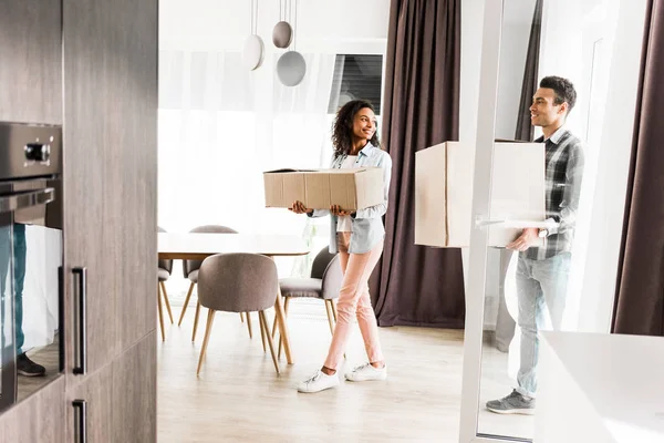 Visão de comprimento total de Africano americano marido e mulher segurando caixas e olhando um para o outro enquanto caminhando em casa — Fotografia de Stock