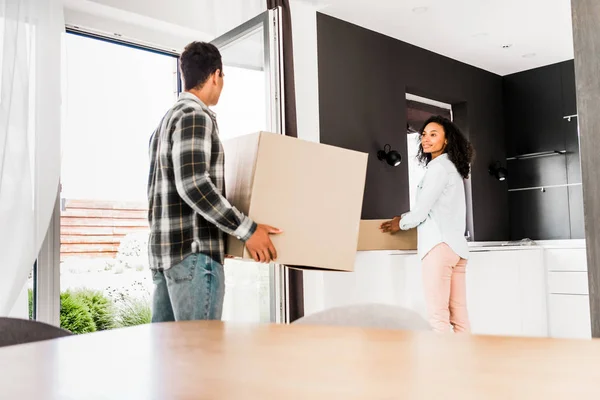 Marido y mujer afroamericanos sosteniendo cajas y mirándose - foto de stock