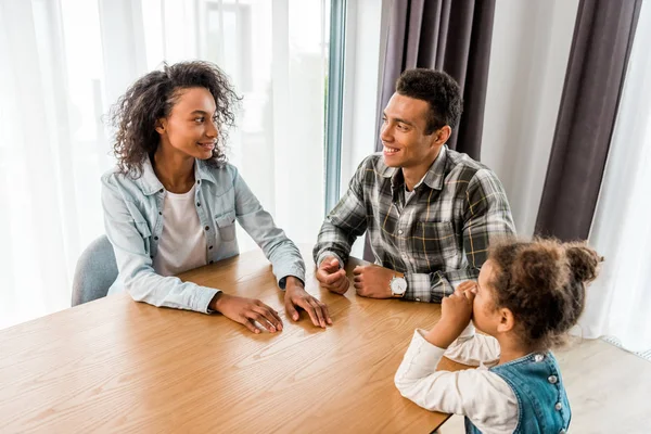 Glückliche afrikanisch-amerikanische Familie sitzt vor Tisch, lächelt und schaut einander an — Stockfoto