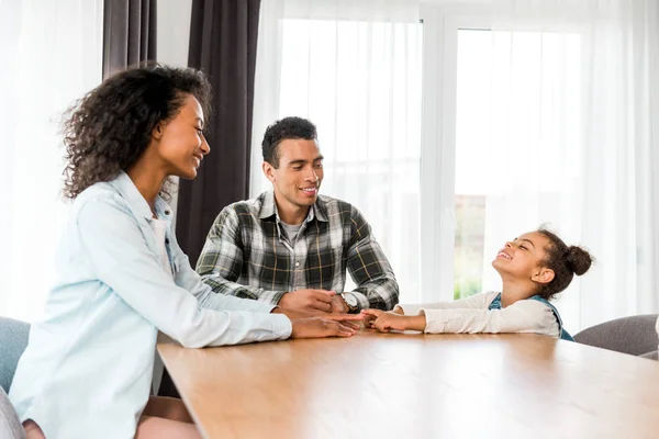 Afrikanisch-amerikanische Familie sitzt vor Tisch, lächelt und schaut einander an — Stockfoto