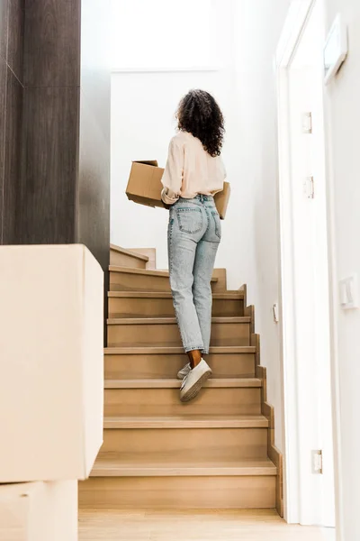 Back view of woman walking upstairs while holding box — Stock Photo