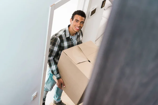 Vista de ángulo alto del hombre afroamericano guapo que sostiene la caja, sonriendo y mirando a la cámara - foto de stock