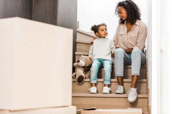 Ganzkörperansicht von Mutter und Kind, die an der Treppe sitzen und einander anschauen — Stockfoto