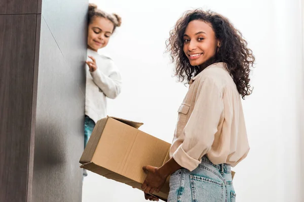 African american woman with box in hand standing on stairs while daughter looking down — Stock Photo