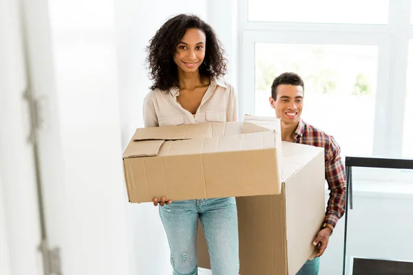 Selective focus of african american woman and man going upstairs with boxes — Stock Photo