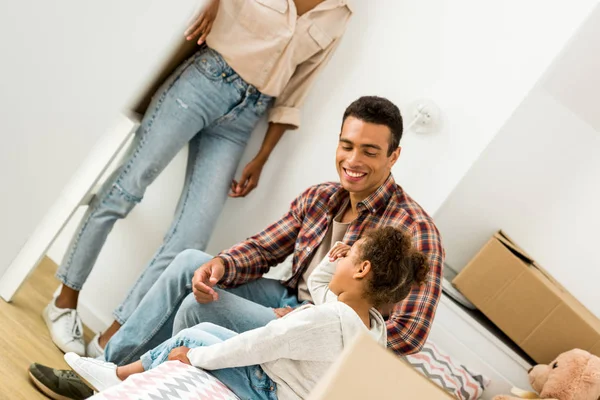 Cropped view of woman standing near wall while african american father smiling and sitting near daughter — Stock Photo