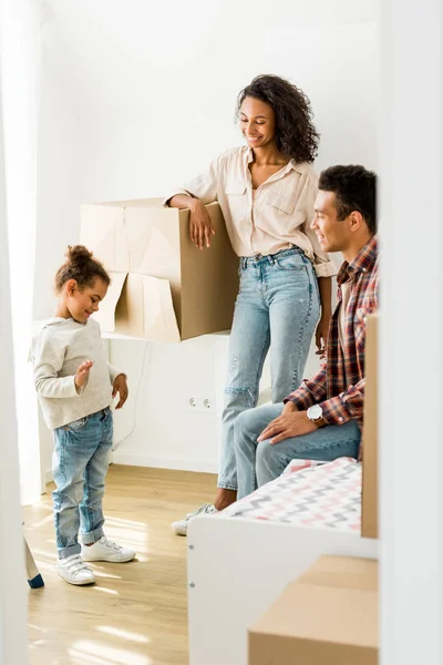 Vista completa de la madre y el padre afroamericanos mirando a la hija - foto de stock