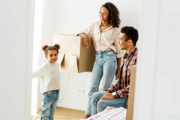 Africano americano mujer apoyándose en caja y hombre mirando niño mientras hija mirando cámara - foto de stock