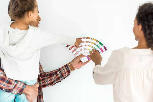 African american family trying to choose color for their wall from colorful palette isolated on white — Stock Photo