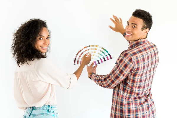 Homem americano africano e mulher tentando escolher a cor para sua parede de paleta colorida e olhando para a câmera isolada no branco — Fotografia de Stock