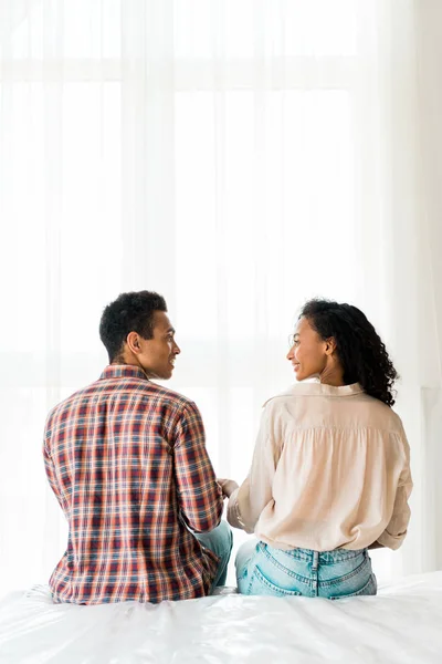 African american husband and wife sitting on bed, holding hands and looking at each other — Stock Photo