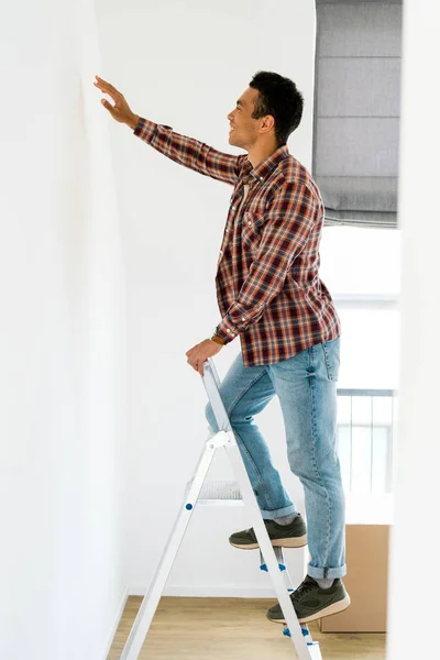 Side view of african american man standing at ladder and looking at wall — Stock Photo