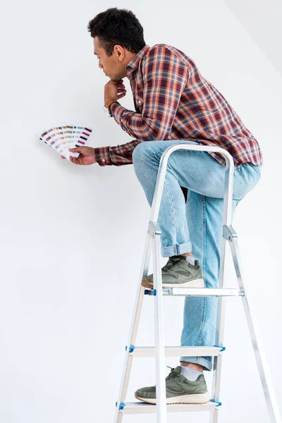 Homem americano africano em pé na escada e olhando para paleta colorida isolado no branco — Fotografia de Stock