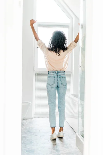 Rückansicht einer Frau, die mit den Händen in der Luft im Badezimmer steht — Stockfoto