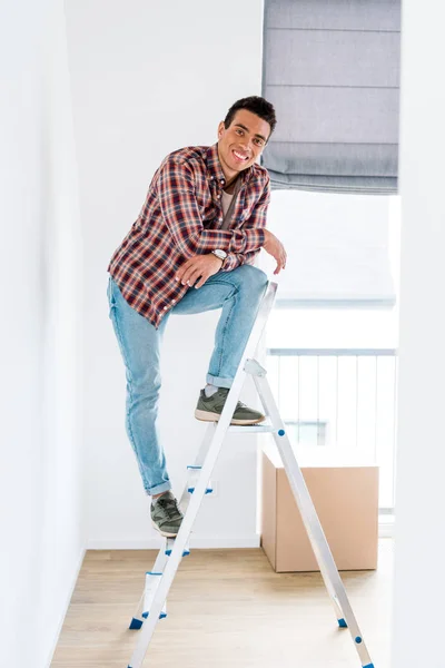 Full length view of handsome african american man standing at step ladder and looking at camera — Stock Photo