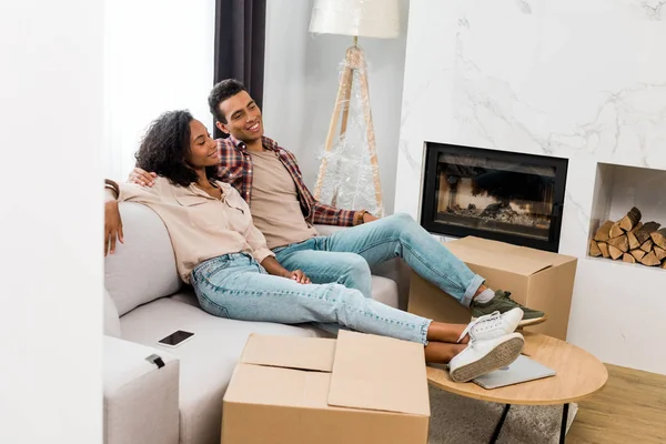 Full length view of african american man and woman relaxing while sitting on sofa and looking away — Stock Photo