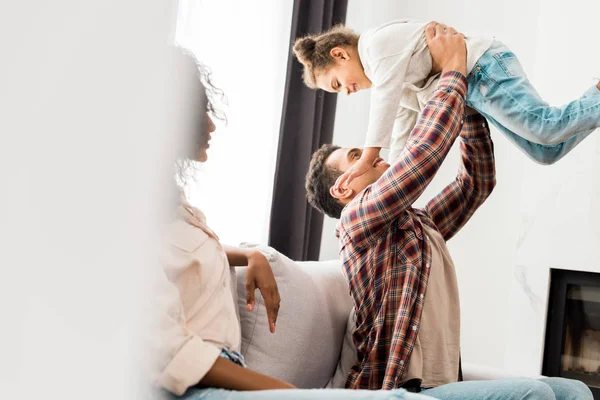 Messa a fuoco selettiva del padre afro-americano che tiene il bambino e la madre guardando il marito — Foto stock